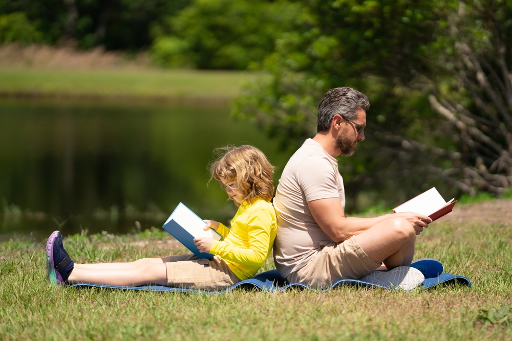 Father,Read,A,Book,With,Son,In,A,Park,Outdoors.